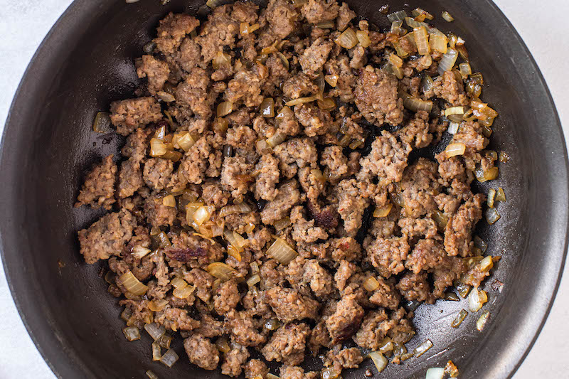 Overhead image of sausage and onion cooked together in a skillet.