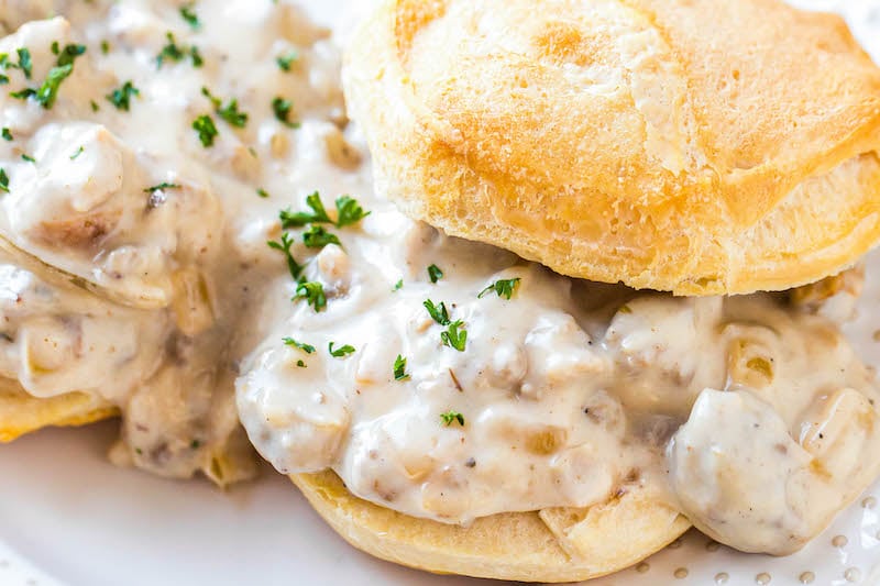 Up close image of sausage gravy served over biscuits with herbs on top.