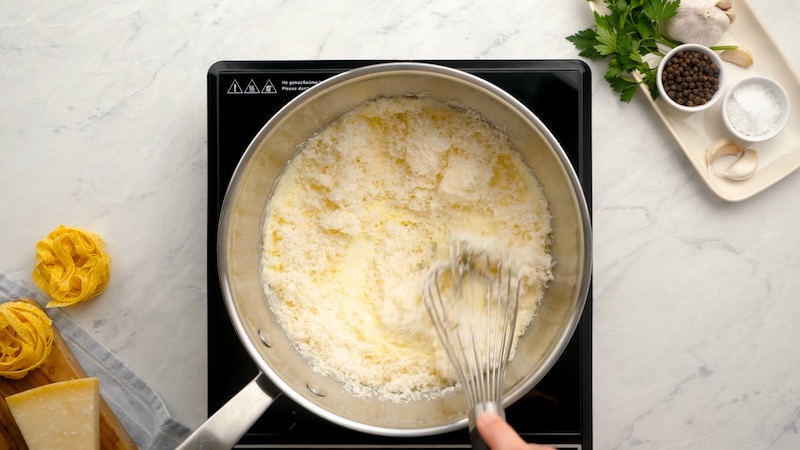 Parmesan cheese being added to a skillet with cream sauce in it.