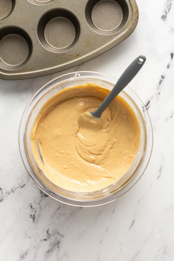 Peanut butter has been mixed into the melted white chocolate in a glass mixing bowl.