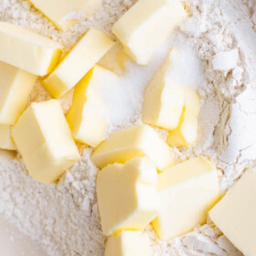 Cubed butter sitting on top of flour in a bowl.
