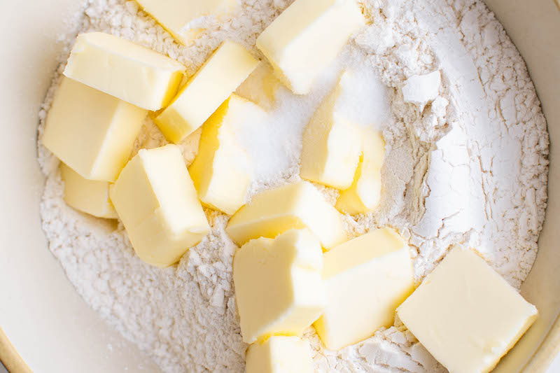 Cubed butter sitting on top of flour in a bowl.