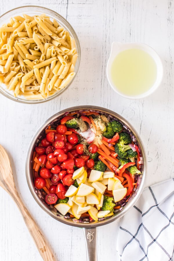 Vegetables in a sauce pan next to a bowl of pasta.