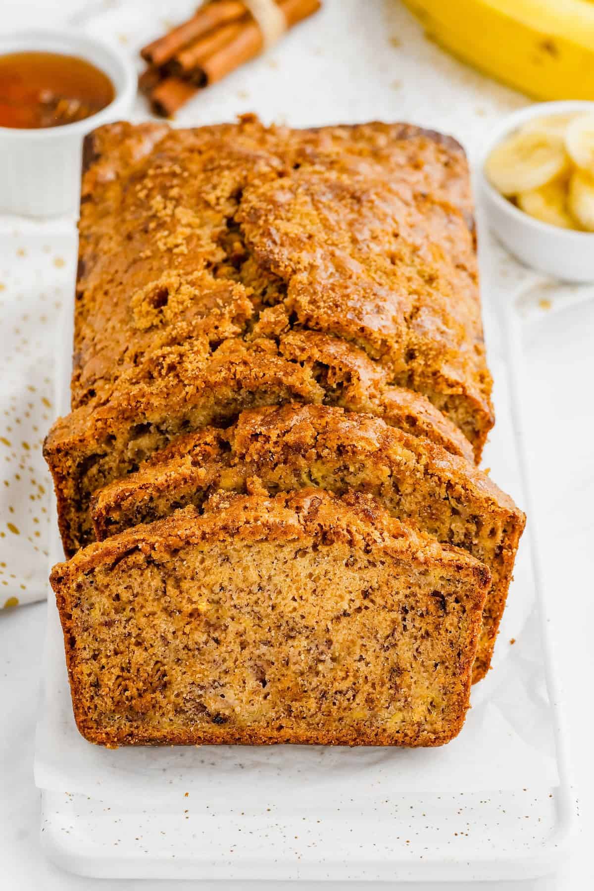 A loaf of banana bread with brown sugar is presented on a white surface.