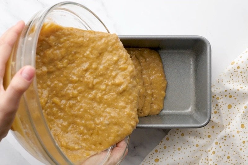 Batter for banana bread being poured into a baking loaf pan.