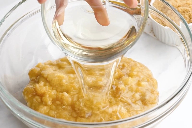 A bowl with mashed banana with oil being poured over the top.