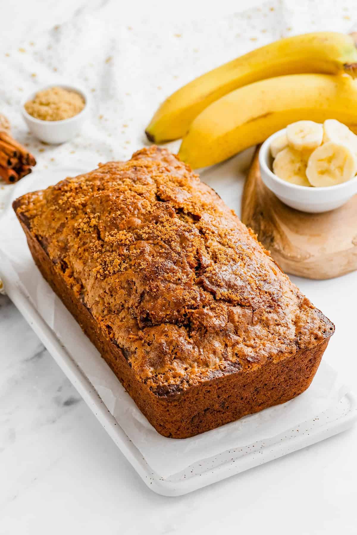 A whole loaf of banana bread with brown sugar presented on a white cutting board.