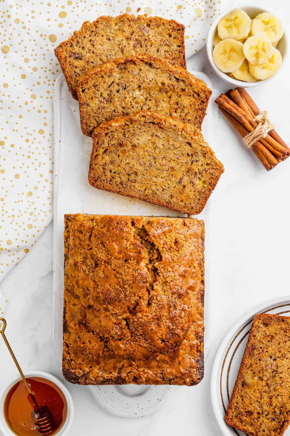 Bananas and cinnamon sticks placed next to slices of homemade banana bread.