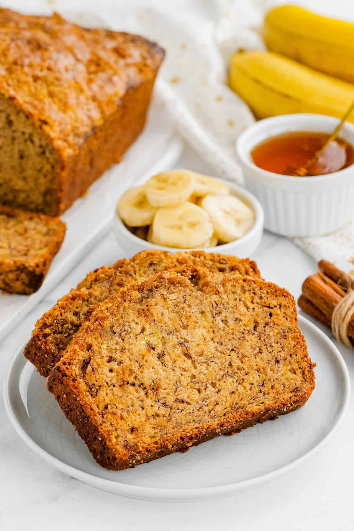 Slices of banana bread with brown sugar topping on a white plate with a loaf of banana bread in the background.