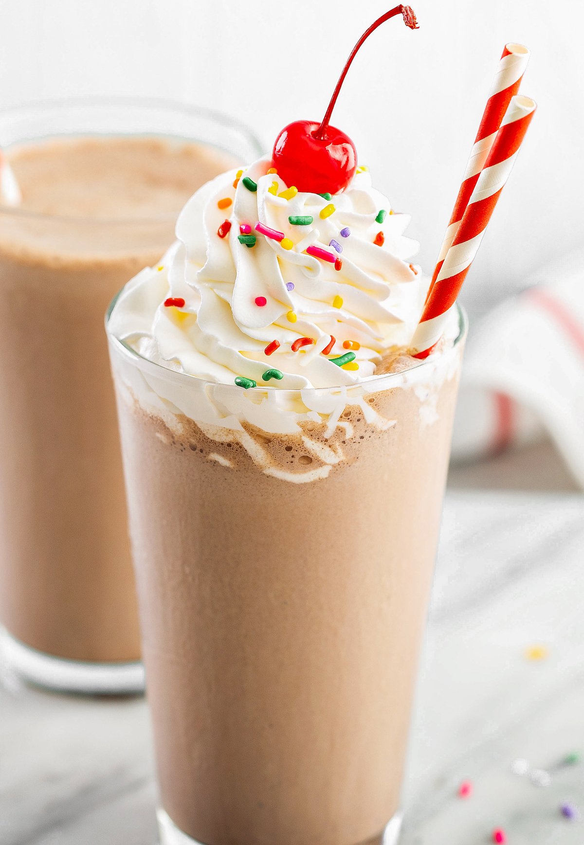 A chocolate milkshake with whipped cream, sprinkles, and a cherry.