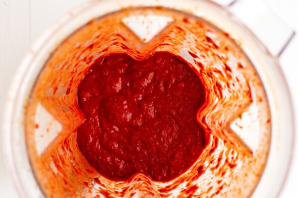 Top view of a blender filled with smooth, thick red sauce or paste with streaks of the mixture visible along the sides of the container.