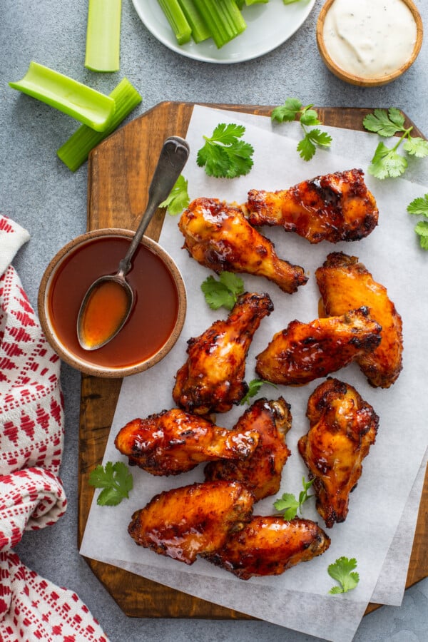 Overhead image of hot honey wings on parchment paper with a bowl of sauce and celery.