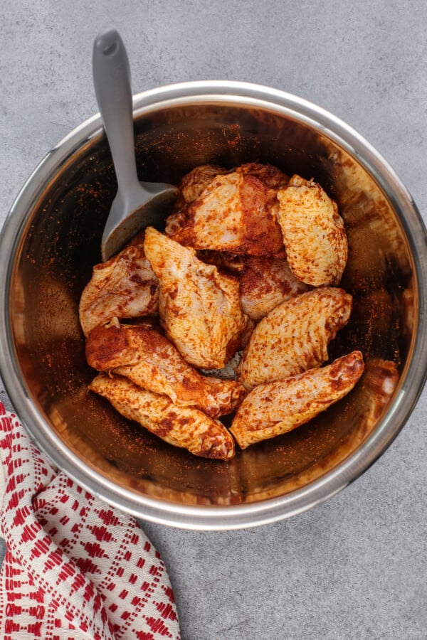 Uncooked chicken wings in a bowl with a spatula covered in sauce. 