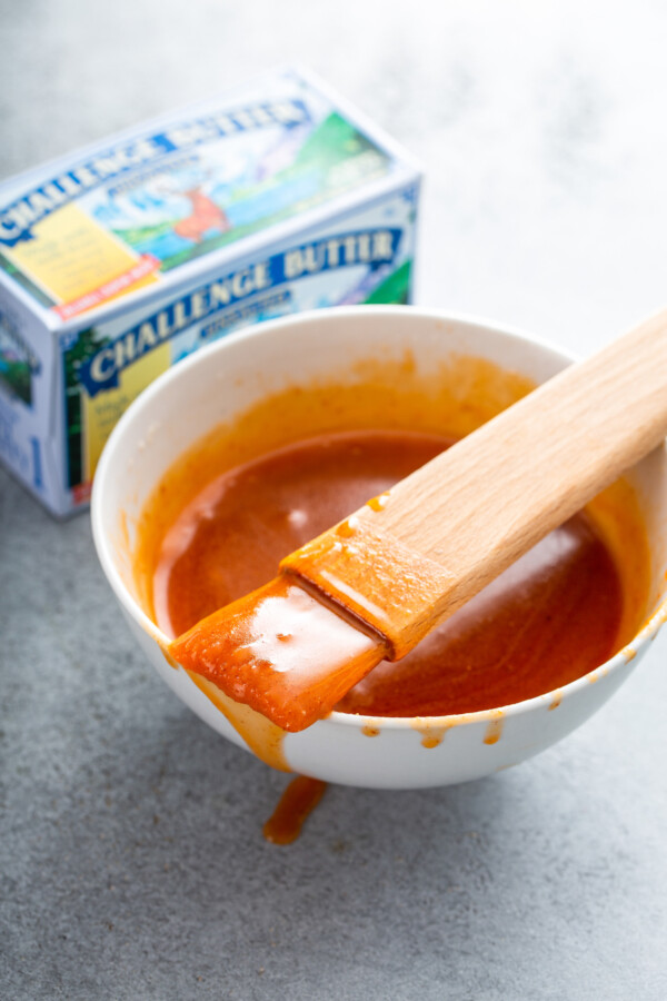 A bowl with sauce and a pastry brush set on top. 