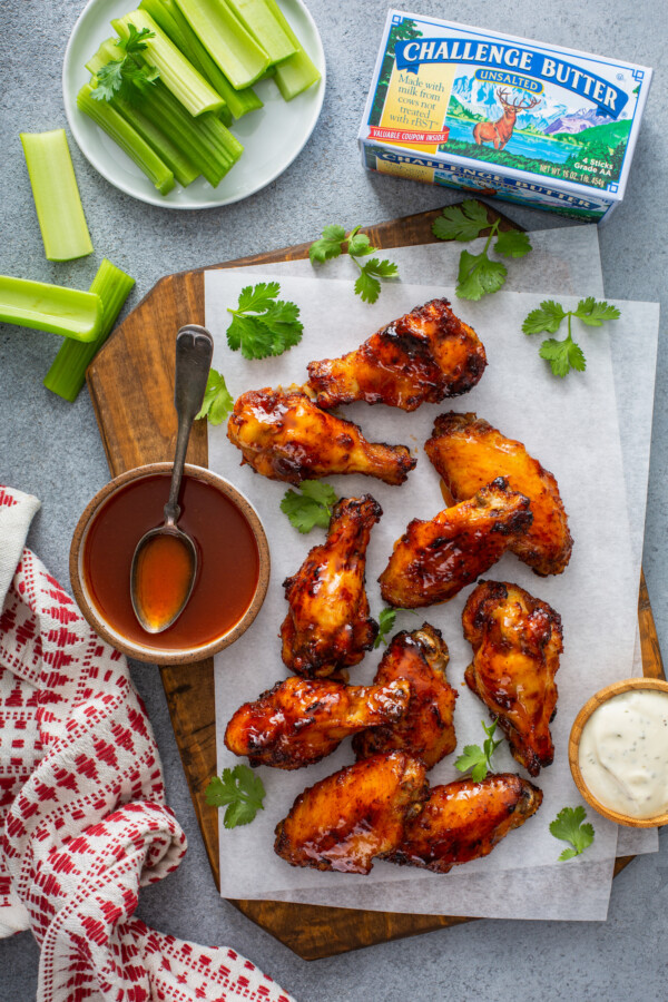 Overhead image of hot honey wings cooked in an air fryer on parchment paper with a bowl of sauce and celery.