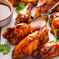 Up close image of air fryer wings covered in hot honey sauce with a spoon pouring extra sauce on top.