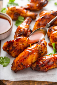 Up close image of air fryer wings covered in hot honey sauce with a spoon pouring extra sauce on top.