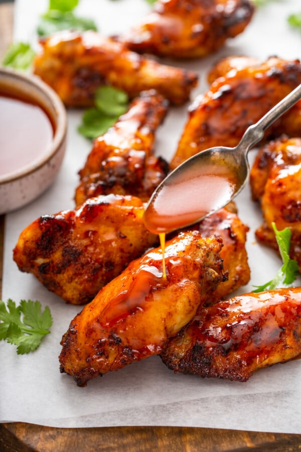 Up close image of air fryer wings covered in hot honey sauce with a spoon pouring extra sauce on top. 
