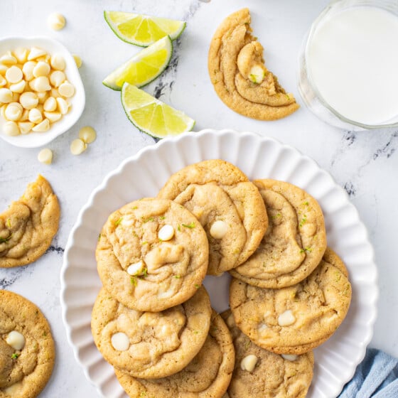 A plate filled with cookies is placed next to several other cookies on a white surface.