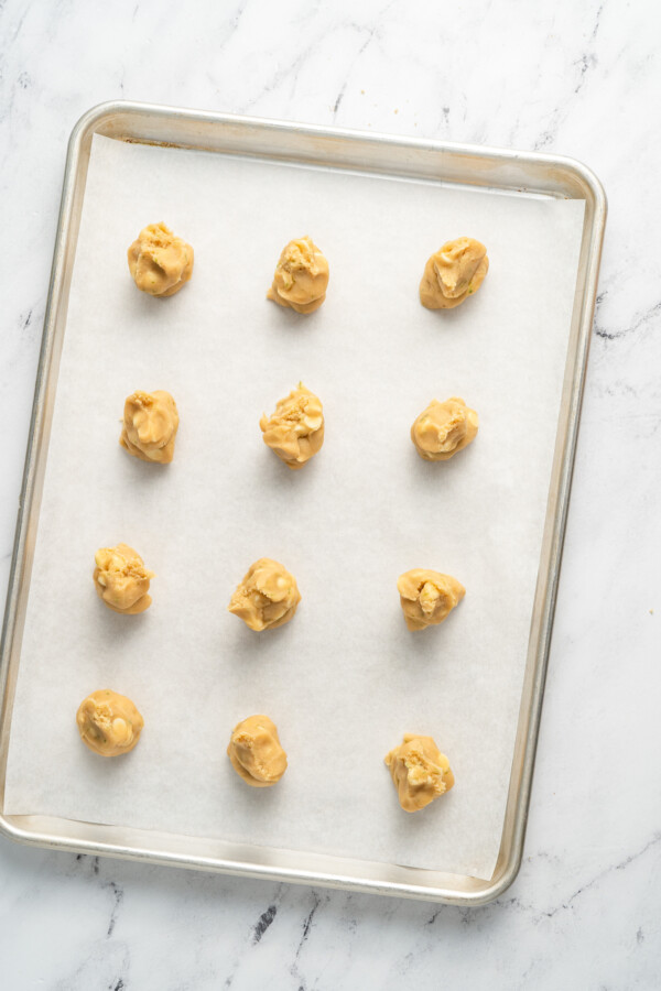 Twelve balls of cookie dough are spread out over a baking sheet.