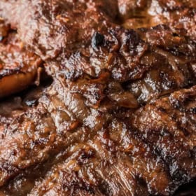 Up close image of a grilled marinated flank steak on a white plate.