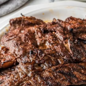 Thin grilled steaks stacked on top of each other on a white plate.