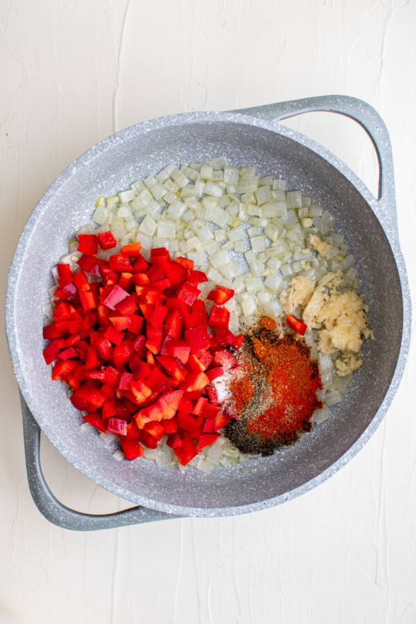 Red bell pepper with onion, garlic and seasonings in a pan.