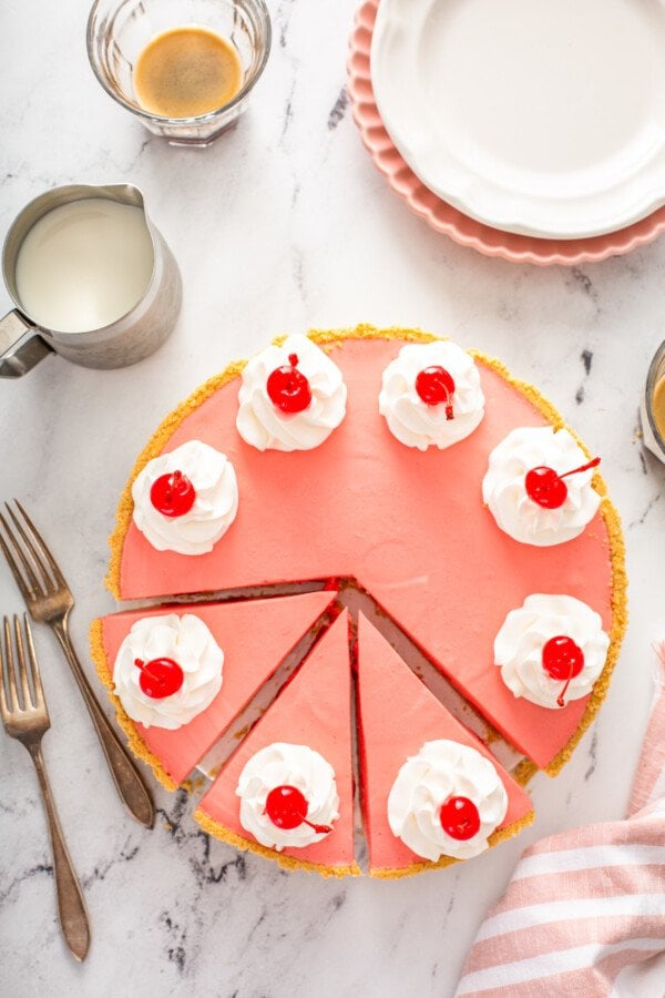 Overhead image of a cherry pie sliced into pieces with plates and forks and knifes. 