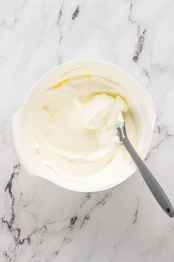 A white bowl filled with whip cream and a spoon on top of a marble countertop. 