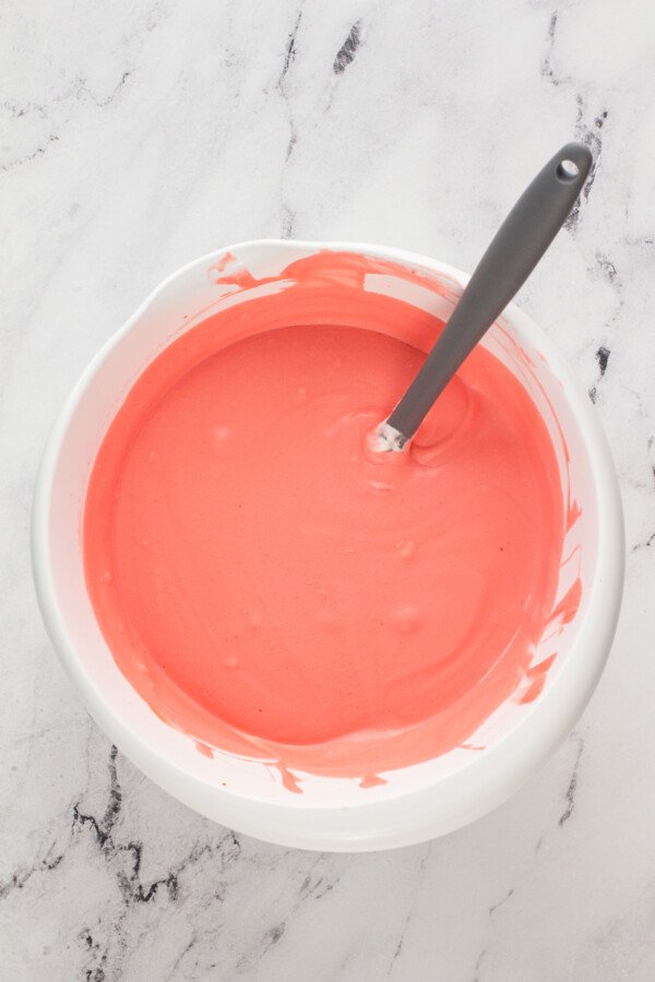 A bowl with cherry cream pie filling with a spoon on a marble countertop. 