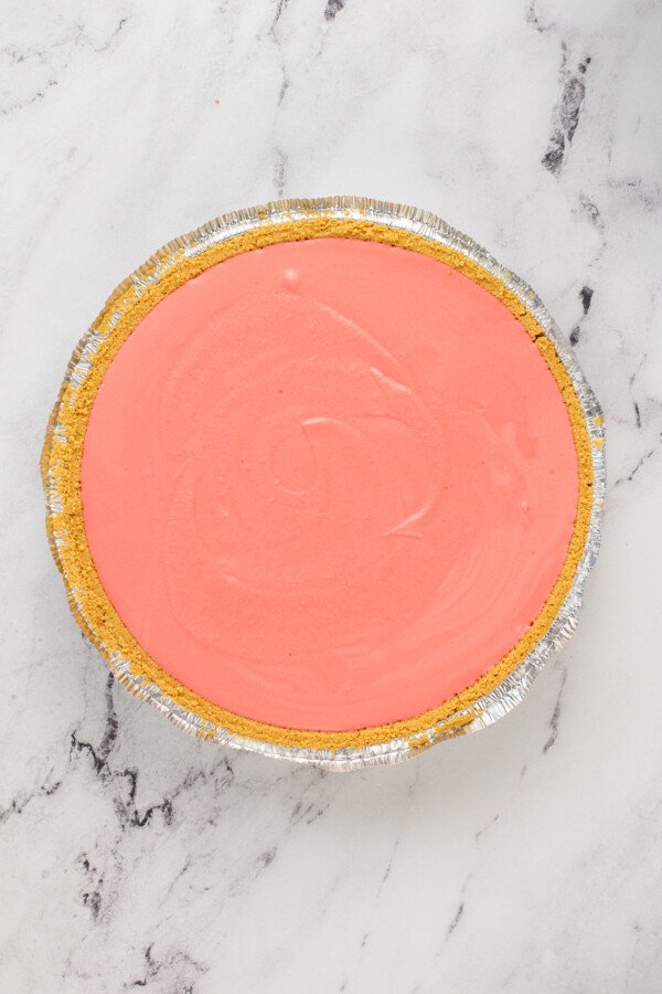 Overhead view of a graham cracker pie crust with a pink filling on marble countertop.