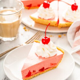 A slice of cherry jello pie on a white plate with the full pie behind it in the background.