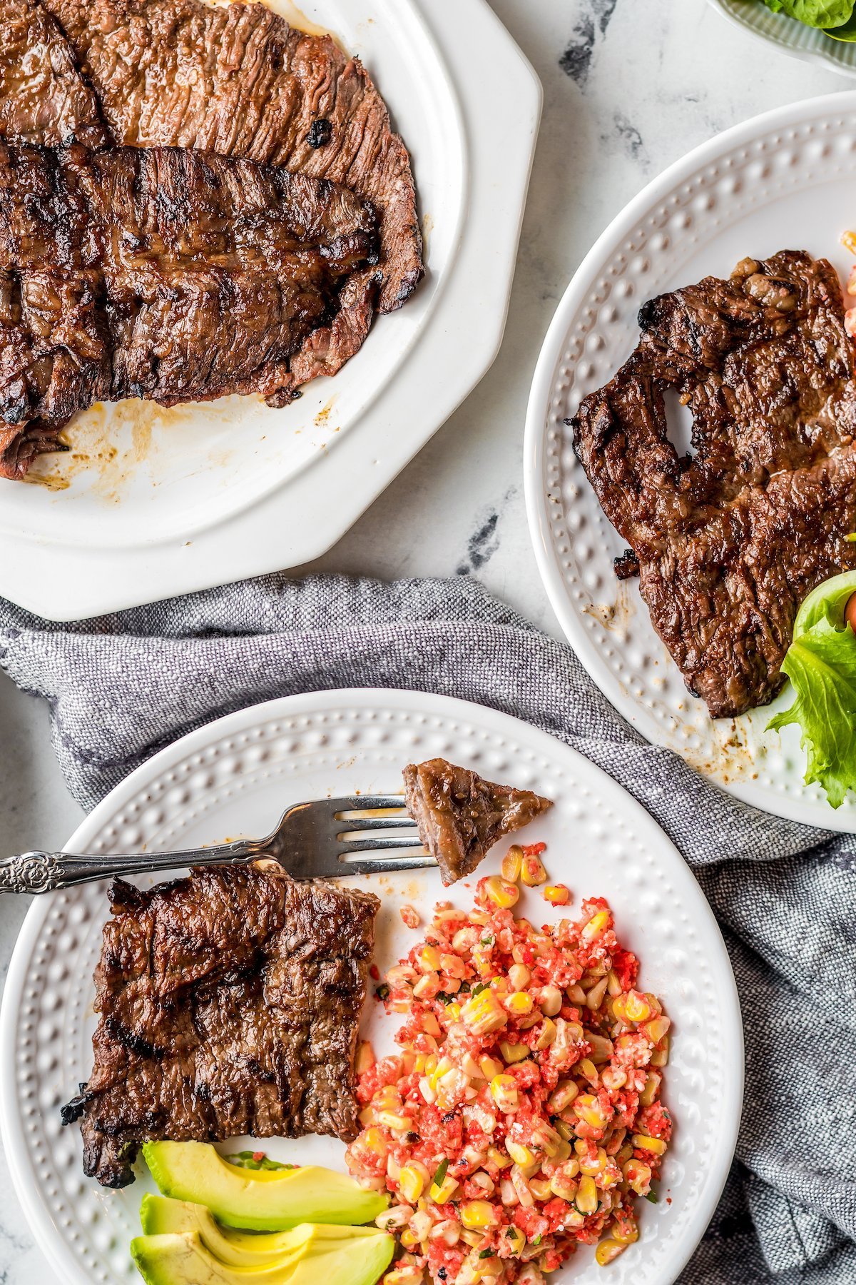 Two plates of flank steak with avocado and side salad.