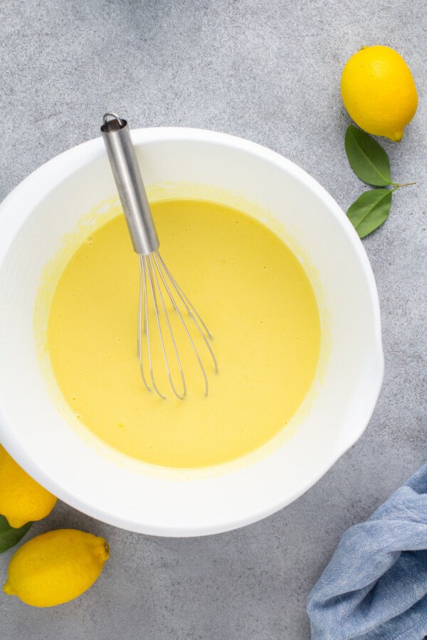 Lemon pudding in a white bowl with a whisk.