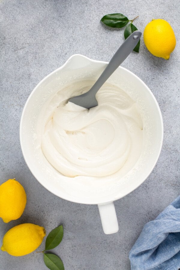Whipped cream in a white bowl with a spatula.