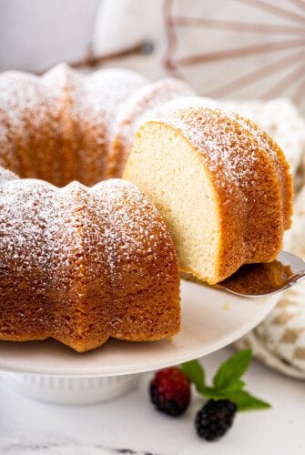 A slice of vanilla bean pound cake on a cake stand with powdered sugar on top.