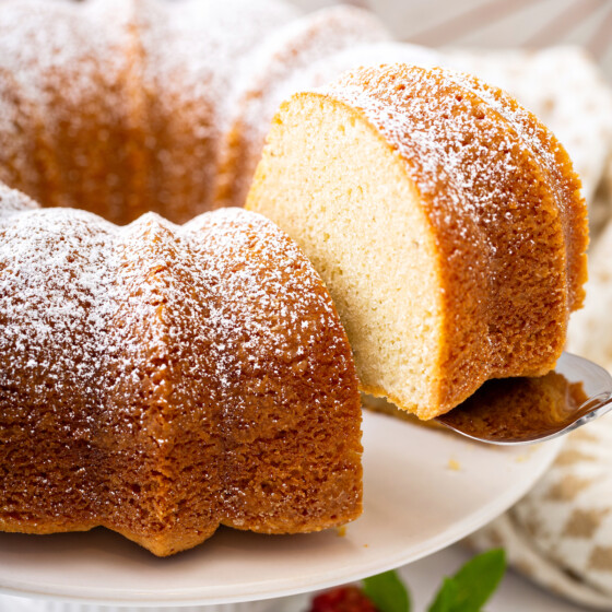 A slice of vanilla bean pound cake on a cake stand with powdered sugar on top.