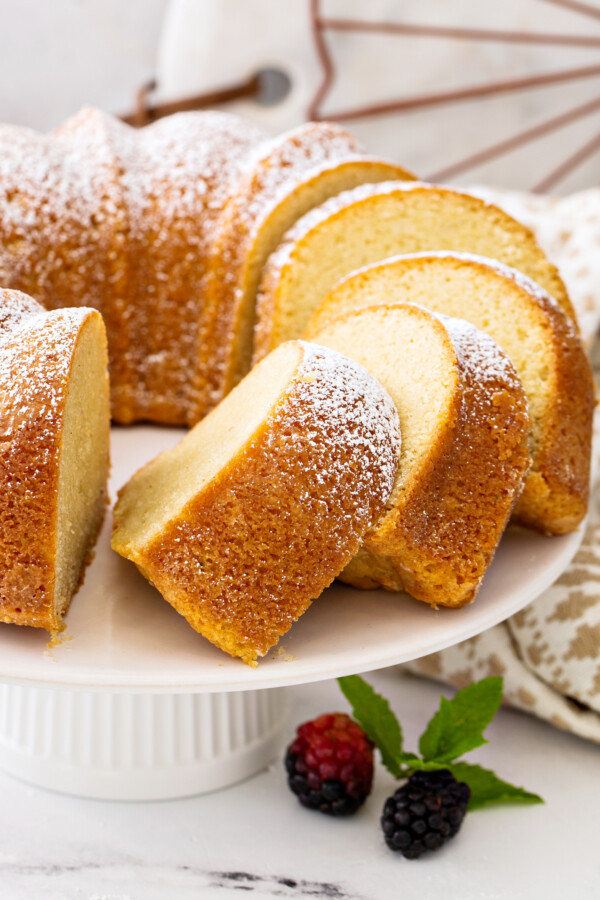 Vanilla Bean Pound Cake on a cake stand sliced into pieces with berries.