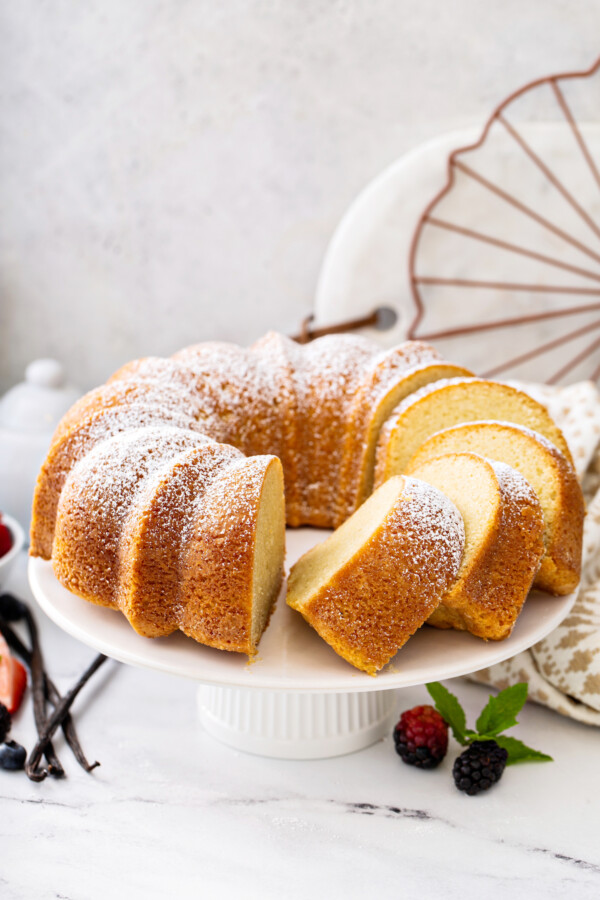 Vanilla pound cake sliced into pieces on a cake stand with vanilla beans. 