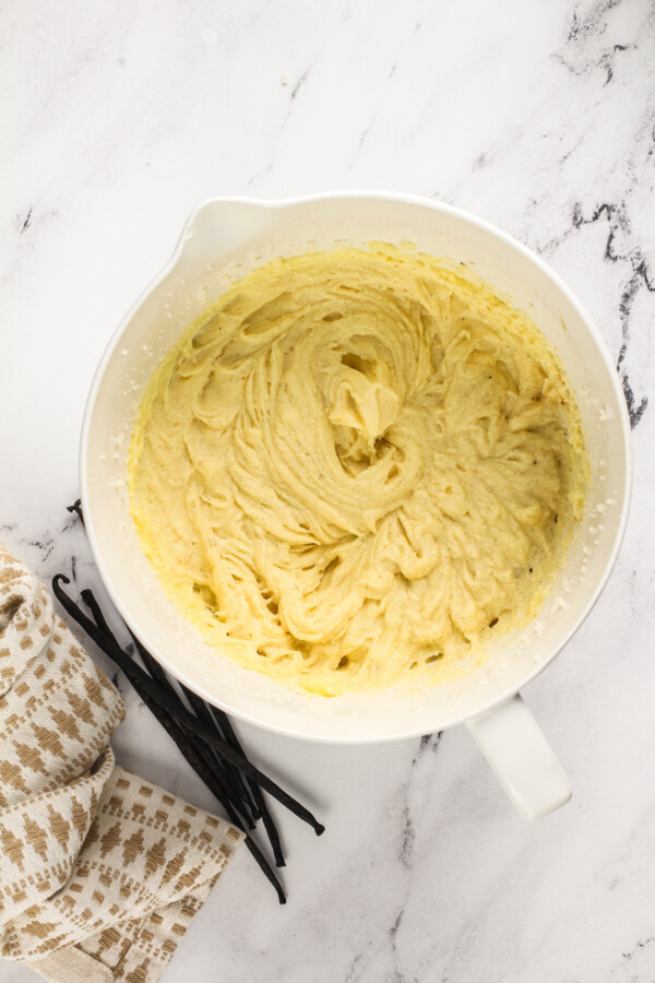 Whipped batter in a mixing bowl with vanilla beans next to the bowl.