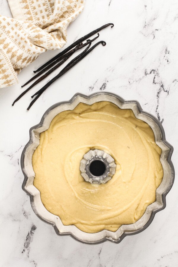 Pound cake batter in a large bundt pan with vanilla beans next to it. 
