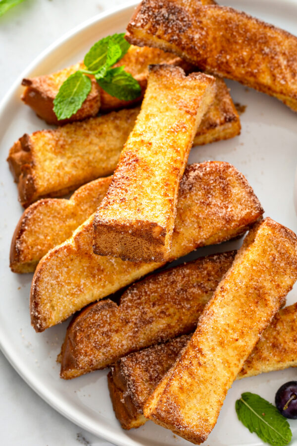 French toast sticks are stacked on a round white plate. 