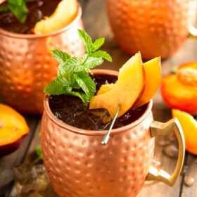 Three copper mugs are filled with peach Moscow mules.