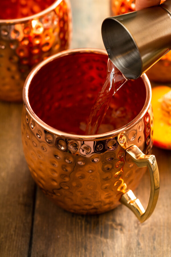 Vodka is being poured into a copper cup. 