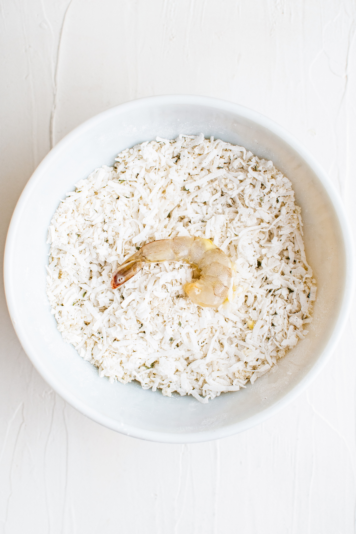 A shrimp coated in egg wash placed in a bowl of coconut and panko mixture.
