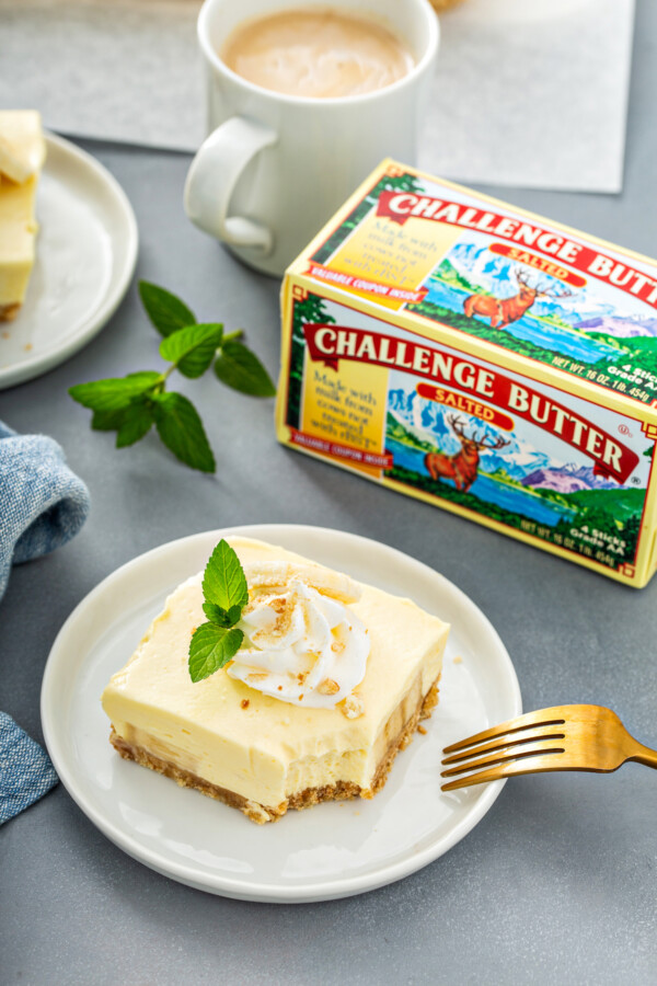A fork is placed on a white plate with a bar of banana pudding next to a box of challenge butter.