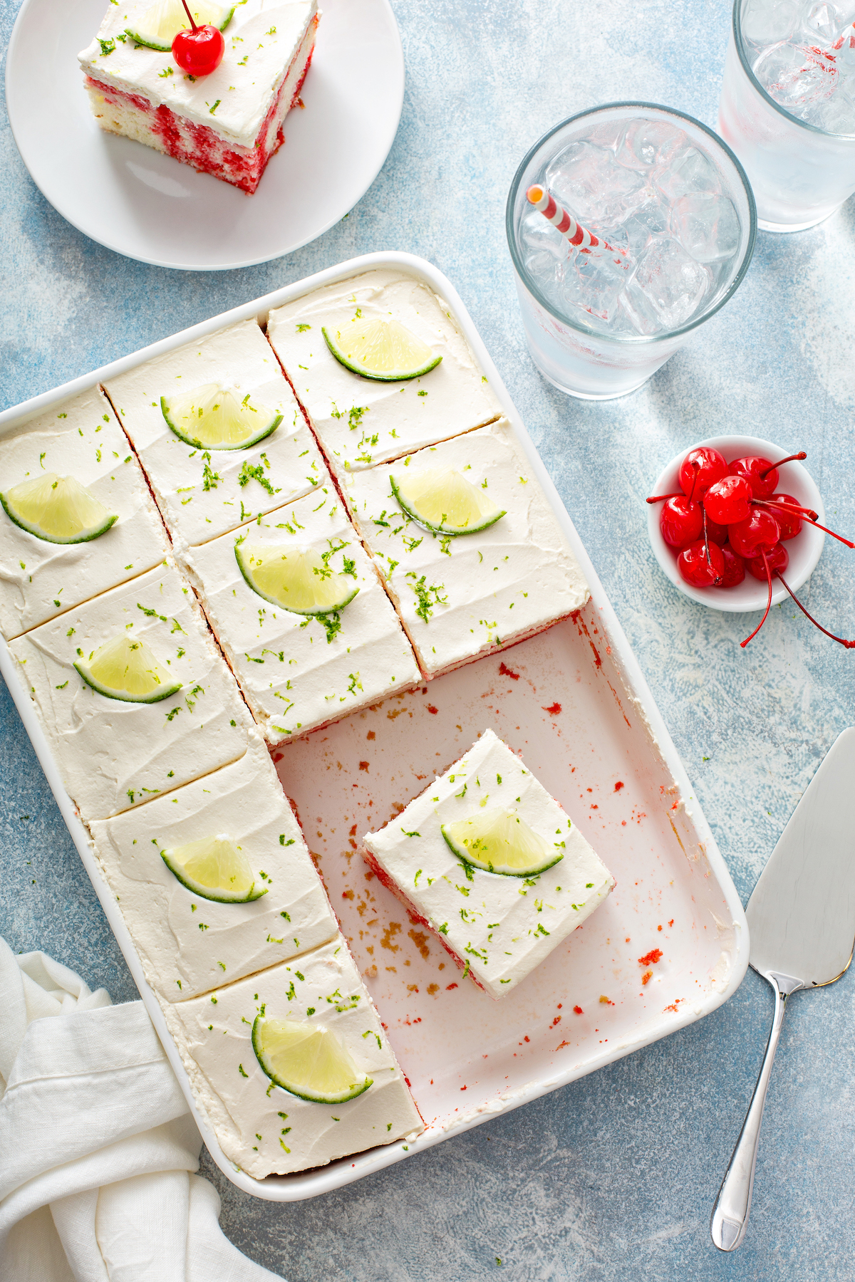 Cherry Lime Poke Cake in a 9x13 casserole with a plate of cherries near by. 