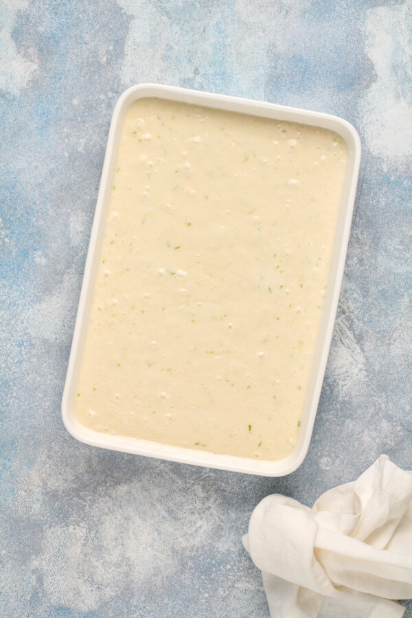 Cake batter poured into a 9x13 pan on a blue background.