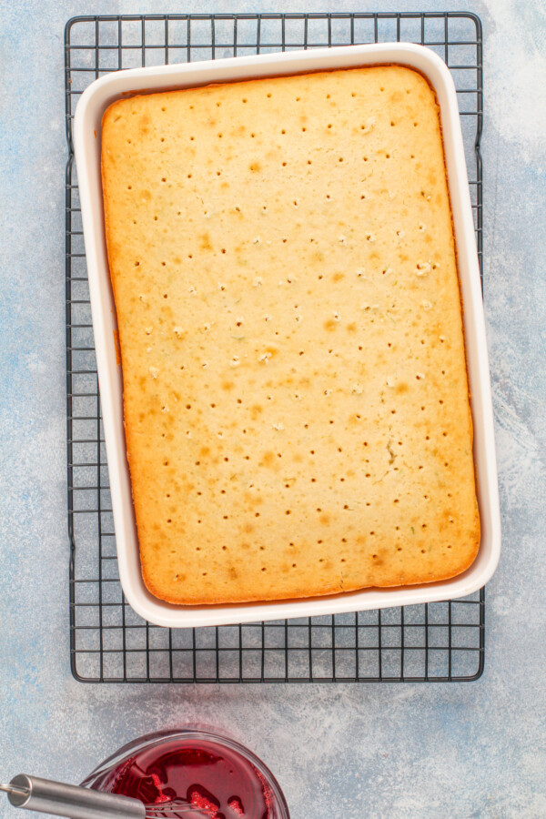 A white cake on a cooling rack with holes poked into it. 