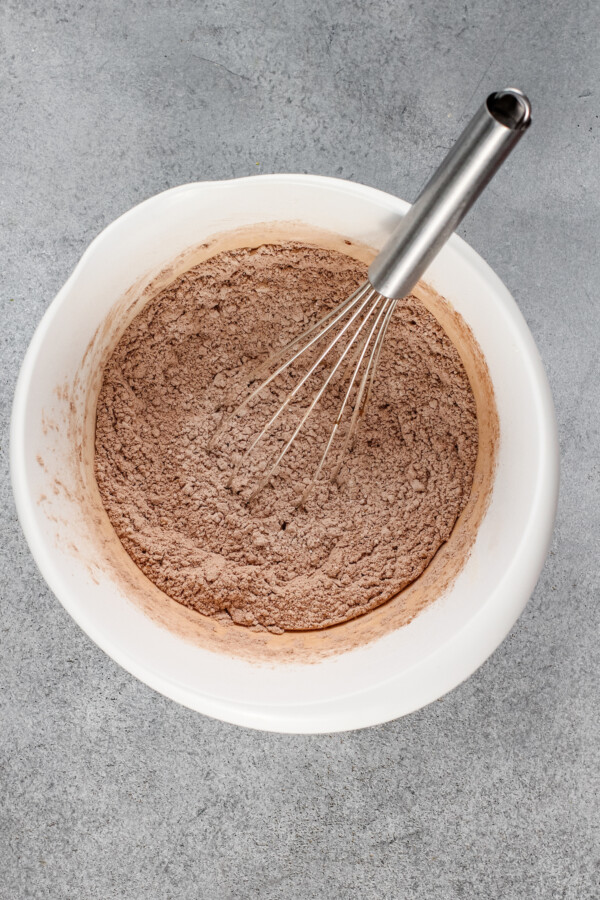 Dry ingredients are being whisked in a white mixing bowl. 